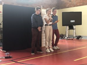 trzech uczniów podczas występu na scenie w hali sportowej