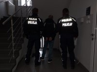 korytarz, mężczyzna tyłem w środku, dwóch policjantów prowadzi zatrzymanego;