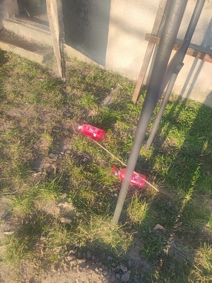 Na ziemi znajdują się dwie czerwone gaśnice. Widać kępy traw.