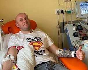 Zdjęcie kolorowe zrobione w szpitalu, w pokoju zabiegowym. Widoczny biały mężczyzna w średnim wieku na łóżku podłączony do aparatury pobierającej szpik kostny.