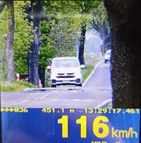 Zdjęcie kolorowe, wykonane miernikiem prędkości przez policjanta. Widoczne białe auto, pod spodem prędkość  wynosząca 116 km/h.