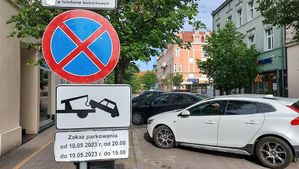 zdjęcie kolorowe, zaparkowane białe auto i tablica informacyjna o zakazie postoju