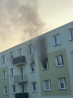 Zdjęcie kolorowe. Wydobywający się dym z dwóch okien budynku wielorodzinnego.