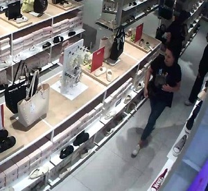 Zdjęcie z monitoringu sklepowego. W oddali kobieta z ciemnymi włosami.