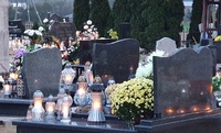 Zdjęcie zdobione na cmentarzu. Widok nagrobków i palących się zniczy.