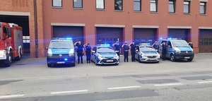 Policjanci przy radiowozach oddają hołd zmarłym strażakom.