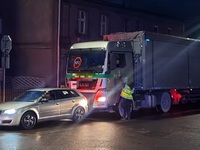 Policjant bada trzeźwość kierującego samochodem ciężarowym. Przed ciężarówką znajduje się auto osobowe.