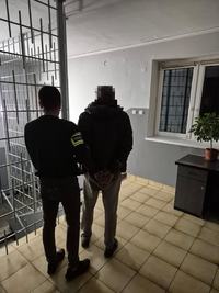 Policjant podczas wykonywanie czynności z zatrzymanym mężczyzną w średnim wieku. Zdjęcie wykonane od tyłu.