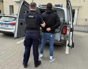 Policjant doprowadza zatrzymanego mężczyznę do radiowozu.