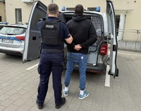 Policjant doprowadza zatrzymanego mężczyznę do radiowozu.