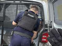 Policjant zamyka drzwi w radiowozie od pomieszczenia dla osób zatrzymanych.