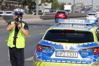 Policjant przy radiowozie mierzy prędkość.