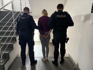Dwóch policjantów podczas doprowadzania zatrzymanej kobiety do radiowozu.