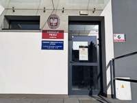 Część budynku Komisariatu Policji w Kłecku z tablicą informacyjną i drzwiami wejściowymi.