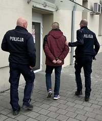 Policjanci podczas doprowadzania do komendy mężczyzny w bordowej kurtce.
