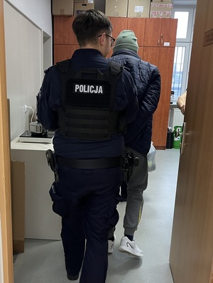Mężczyzna doprowadzany przez policjanta na czynności służbowe.