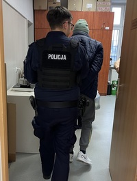 Mężczyzna doprowadzany przez policjanta na czynności służbowe.