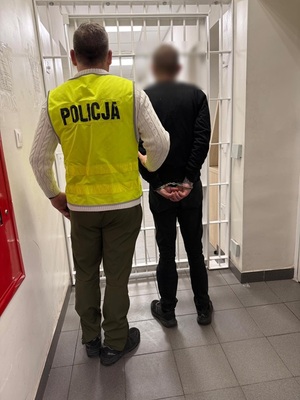 Policjant z zatrzymanym. Zdjęcie wykonane na tle policyjnej kraty.