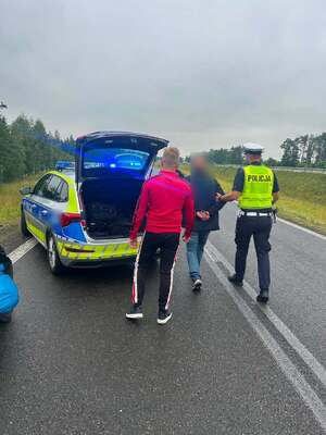 Policjant w kamizelce odblaskowej podczas kajdankowania nietrzeźwego motorowerzysty.