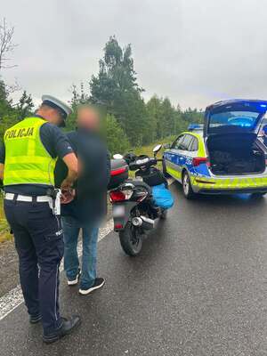 Policjant w kamizelce odblaskowej podczas kajdankowania nietrzeźwego motorowerzysty.
