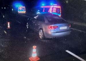 Ciemne auto osobowe na drodze, w pobliżu dwie karetki.